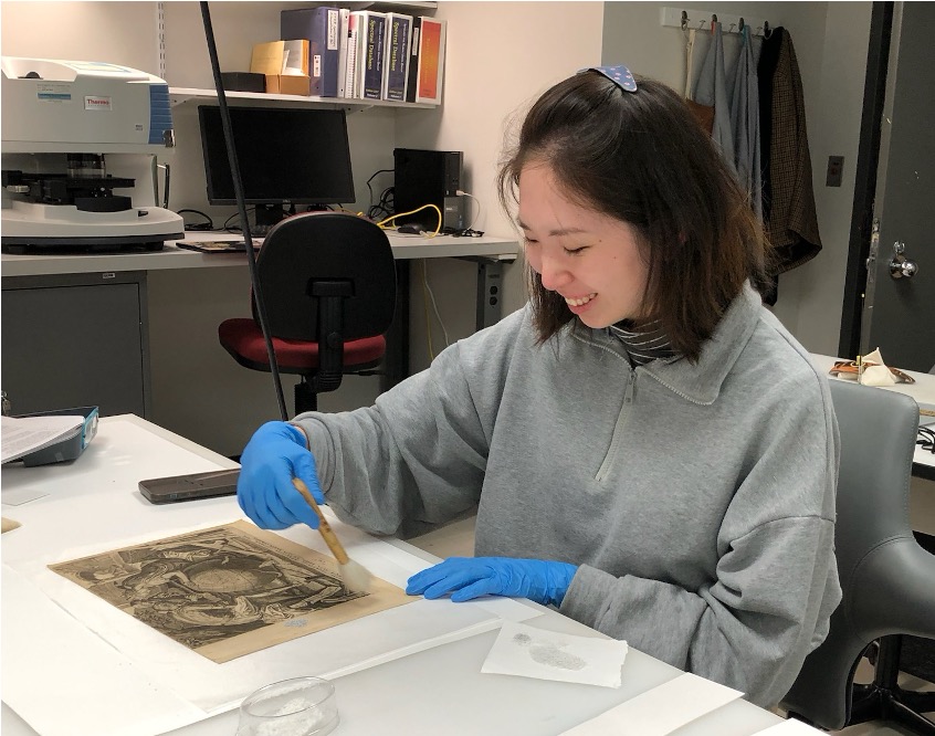 Xu sitting at a table examining and treating an engraving on paper