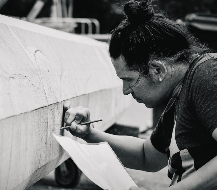 Black and white photo of artist Nicholas Galanin drawing on a large materials in front of him 